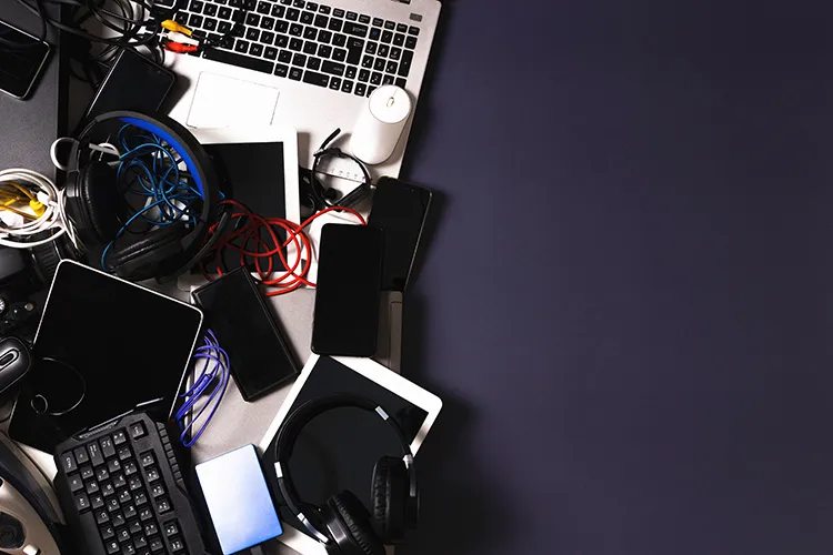 pile of computers, laptops, phones, cords, and headphones