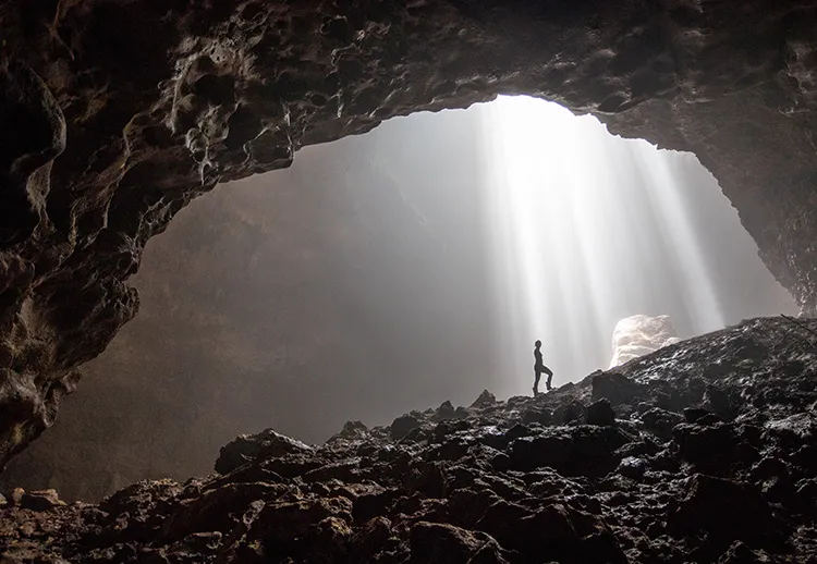 figure standing beneath the light coming in from a save hole