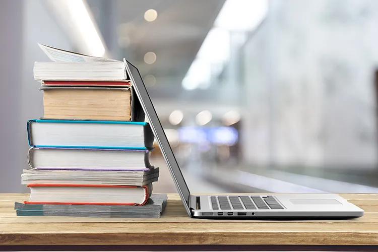 stack of books leaning against a laptop