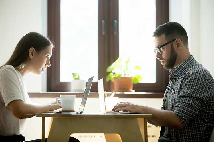 a man and a woman stare at each other while typing on their computers