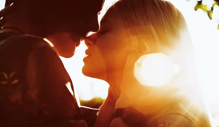 man and woman lean into a kiss with the sun shining in their faces