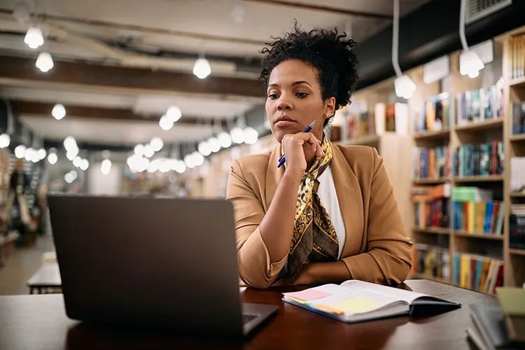 university professor looking at her laptop in a library