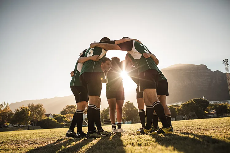 male rugby players huddle in a circle on the field