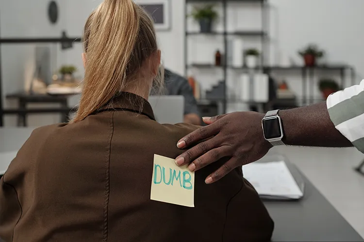 Person putting a sticker with the word dumb on the back of a colleague
